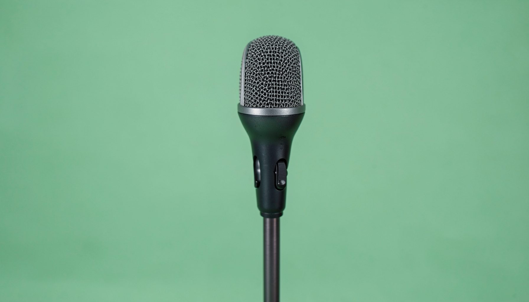A simple microphone on a stand against a soft green background, calm and minimal in mood